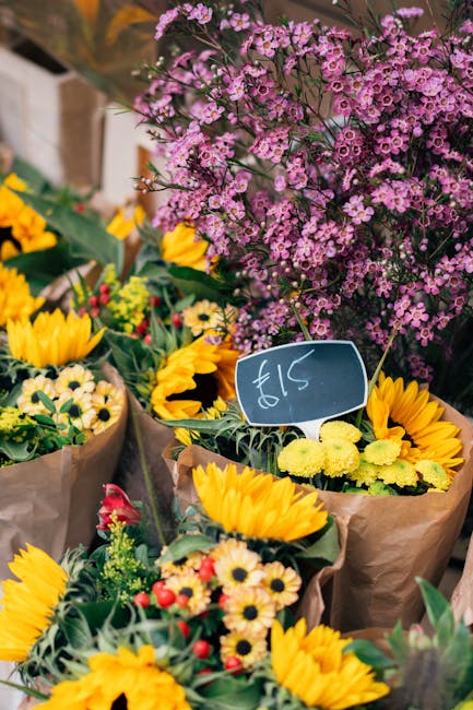 A vibrant selection of fresh floral bouquets displayed at a market stall, featuring bright yellow sunflowers, small white daisies with yellow centers, and clusters of pink and purple waxflowers arrang