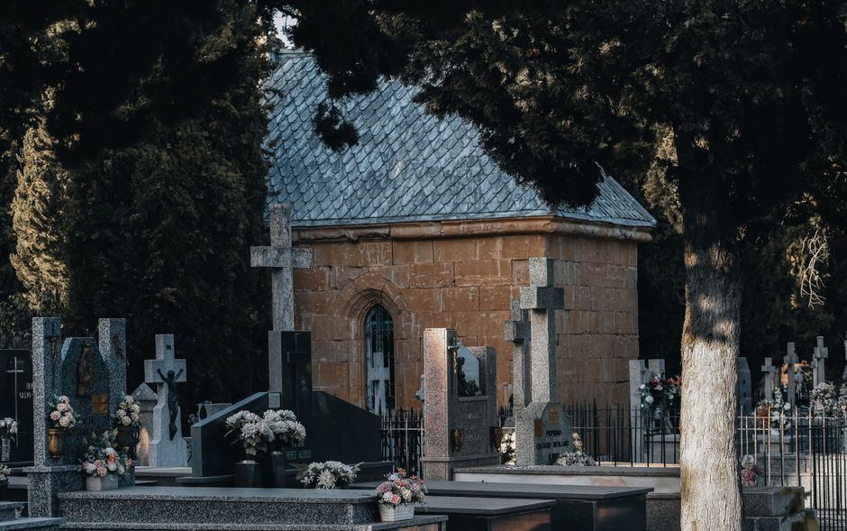 A serene cemetery scene featuring a variety of funeral flowers arranged in bouquets and floral displays placed on and around gravestones made of polished granite and marble. The arrangements include d