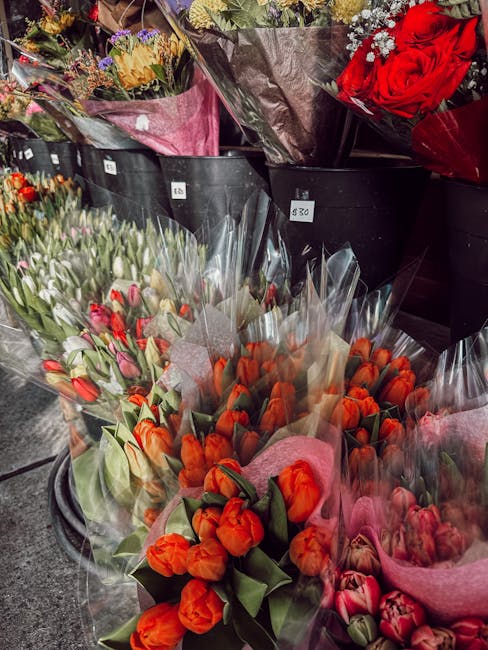 A display of fresh flower bouquets arranged in black crates outside West Kensington florist, featuring tulips in vibrant shades of orange, pink, and red, wrapped in clear and pink tissue paper. Behind