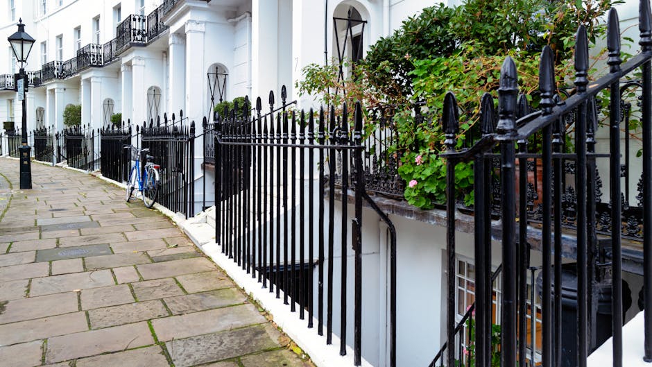 Photograph of a residential street with a paved sidewalk made of rectangular stone tiles, leading past white Georgian-style terraced houses. The houses feature black wrought iron railings along the fr